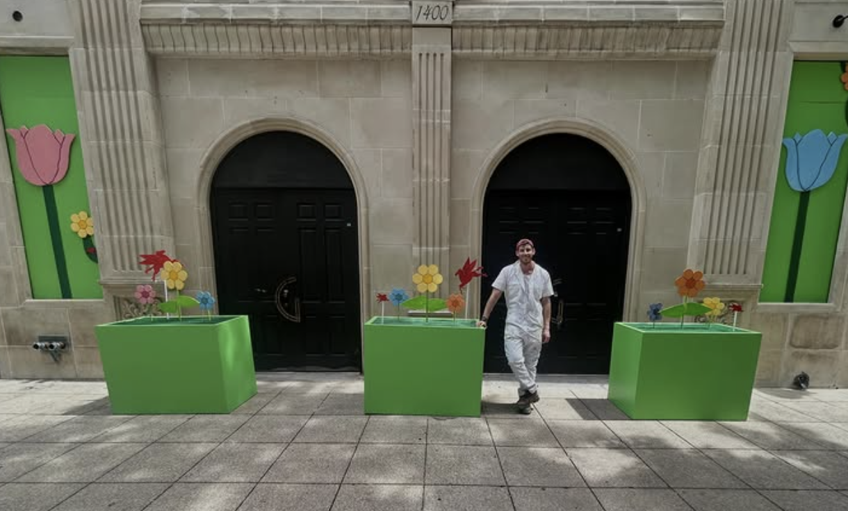 Bright green planter boxes with oversized colorful flowers and red Pegasus accents outside a downtown Dallas building